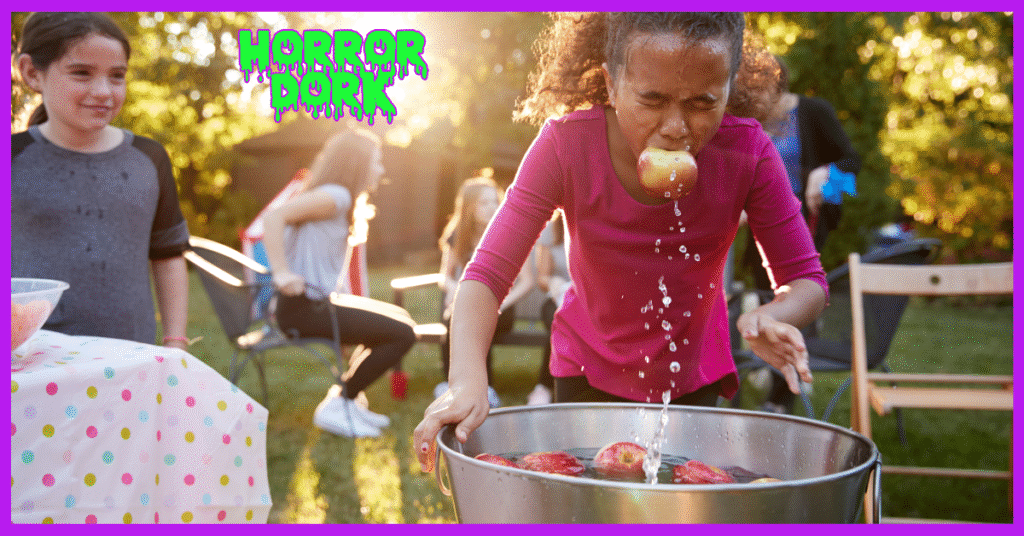 hild bobbing for apples at a Halloween party, biting an apple from a water-filled tub as friends watch and laugh